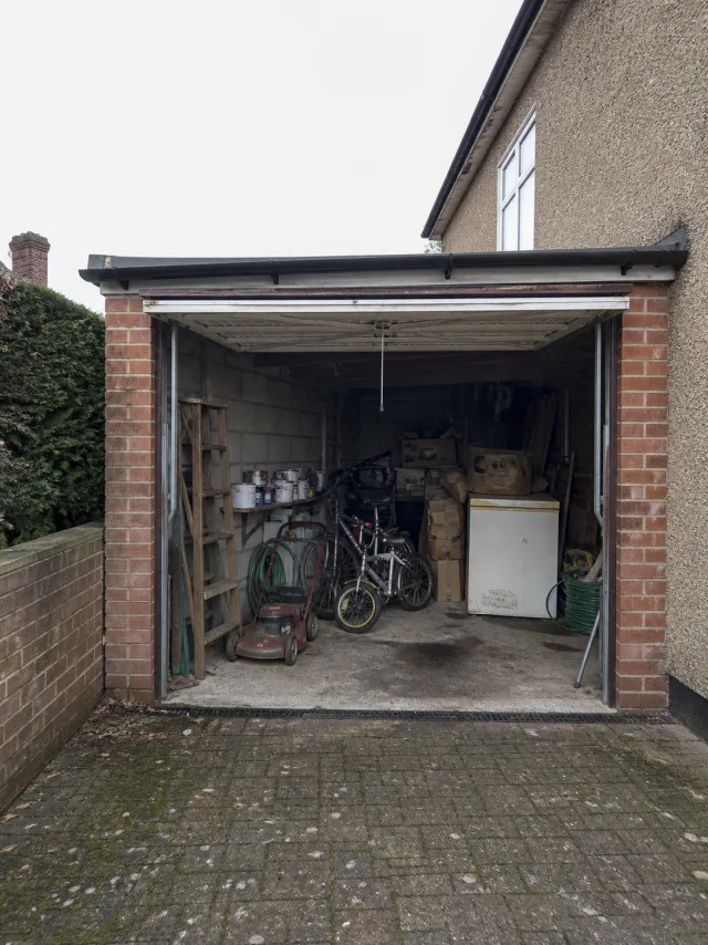 An open single garage in Amersham filled with a ladder, bicycles, paint tins, boxes and an old chest freezer