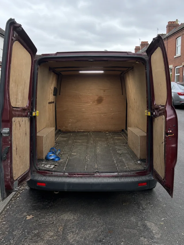 The empty ply-lined load area of a burgundy panel van with both rear doors open